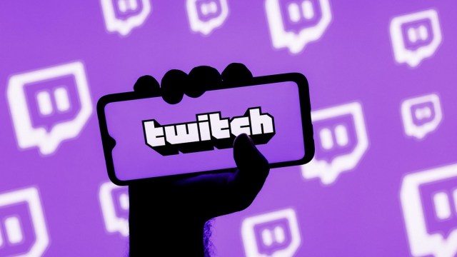 A hand holding a phone with the Twitch logo on the screen.