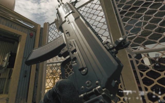 An MW3 player inspecting a black assault rifle against a wire fence. 