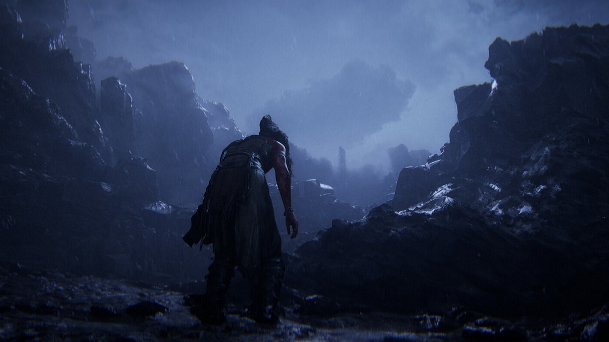 Hellblade 2: Senua walking through a rain-soaked and dark, rocky area.