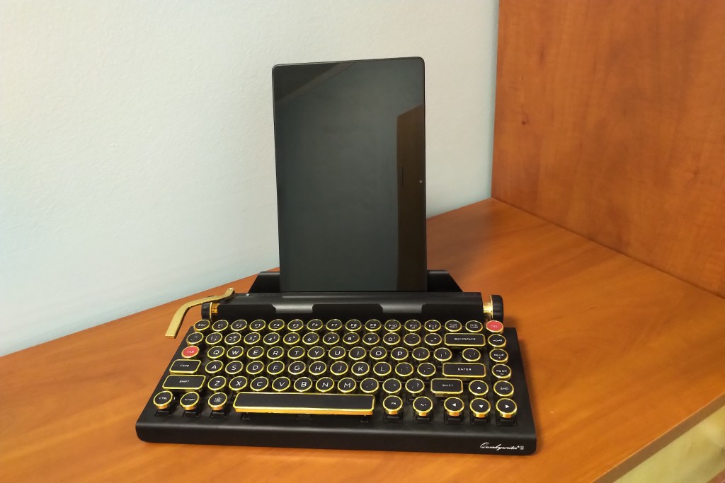 A black-and-gold typewriter-shaped mechanical keyboard with a tablet resting on it