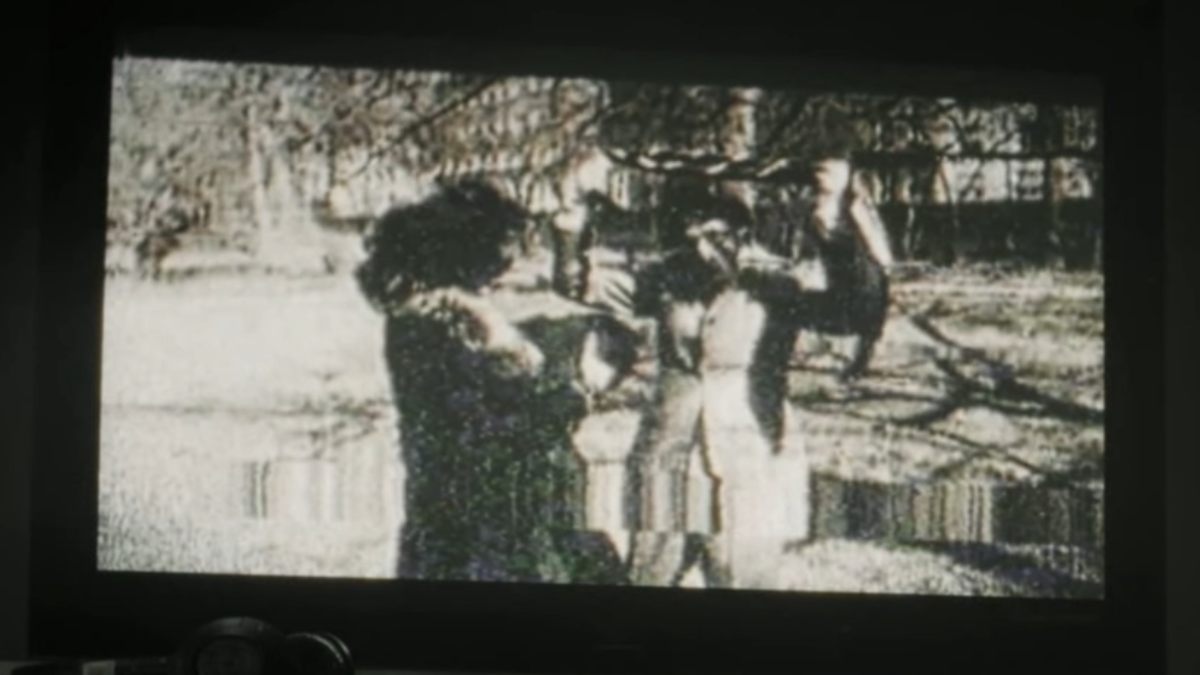Black and white glitched image on VHS tape of man with his hands up, smiling next to a woman who's looking at him